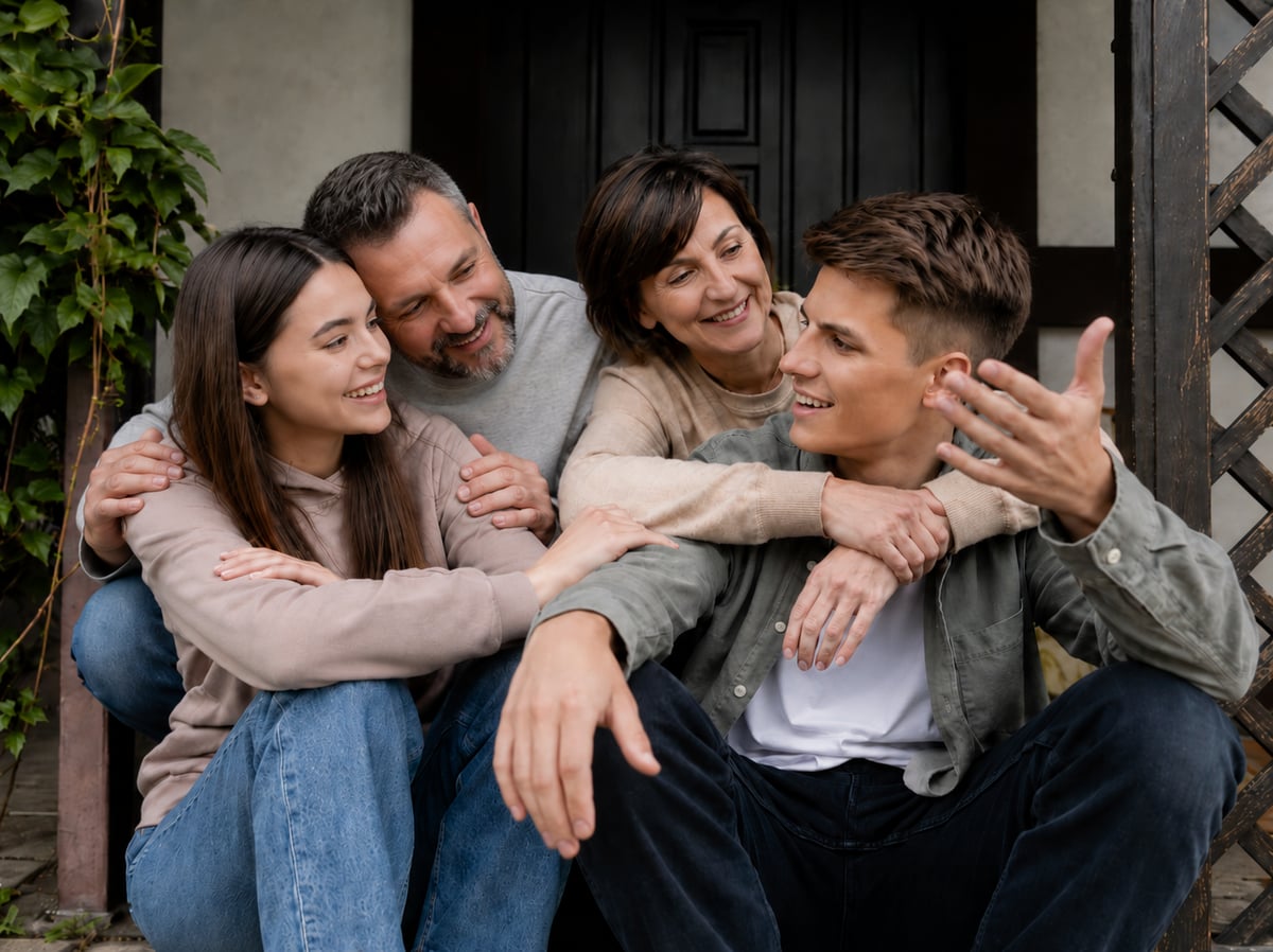 Parents and their two teenagers sitting on the front steps, talking and laughing.